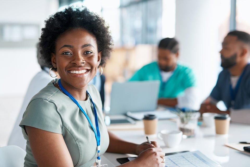 An African American healthcare administrator smiles at the camera while working at a table with other healthcare professionals.