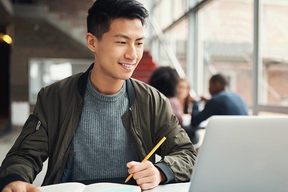 Student working on online business degree on laptop in an open area.